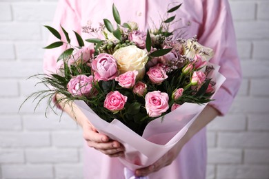 Woman with bouquet of beautiful roses near white brick wall, closeup