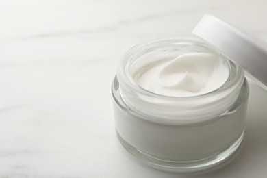 Glass jar of face cream on white marble table, closeup. Space for text