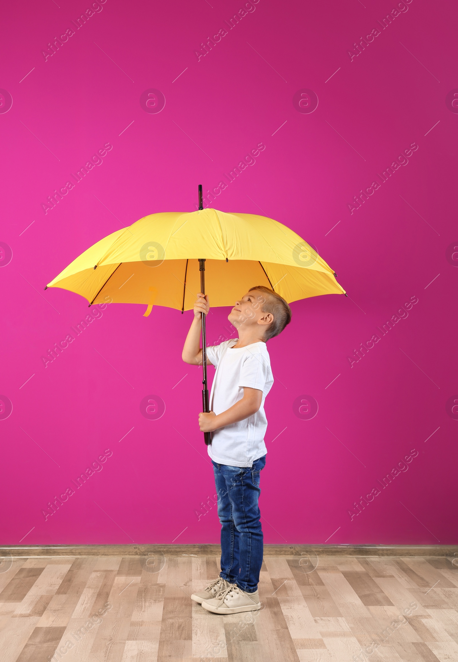 Photo of Little boy with yellow umbrella near color wall