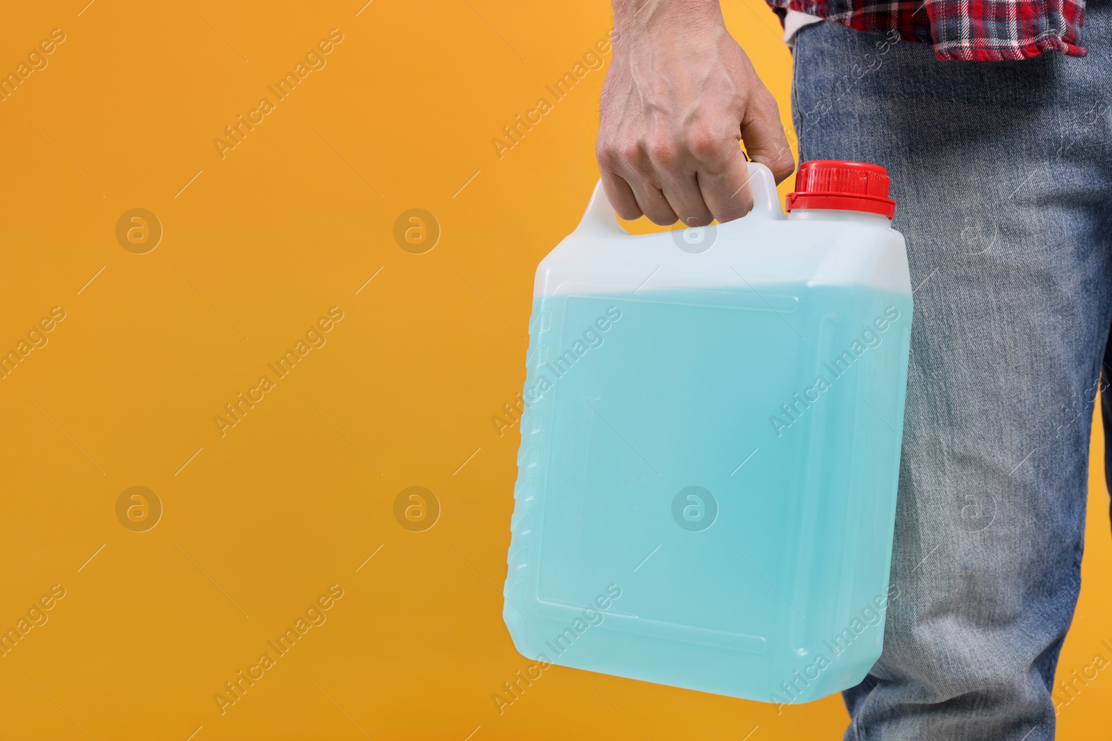 Photo of Man holding canister with blue liquid on orange background, closeup. Space for text