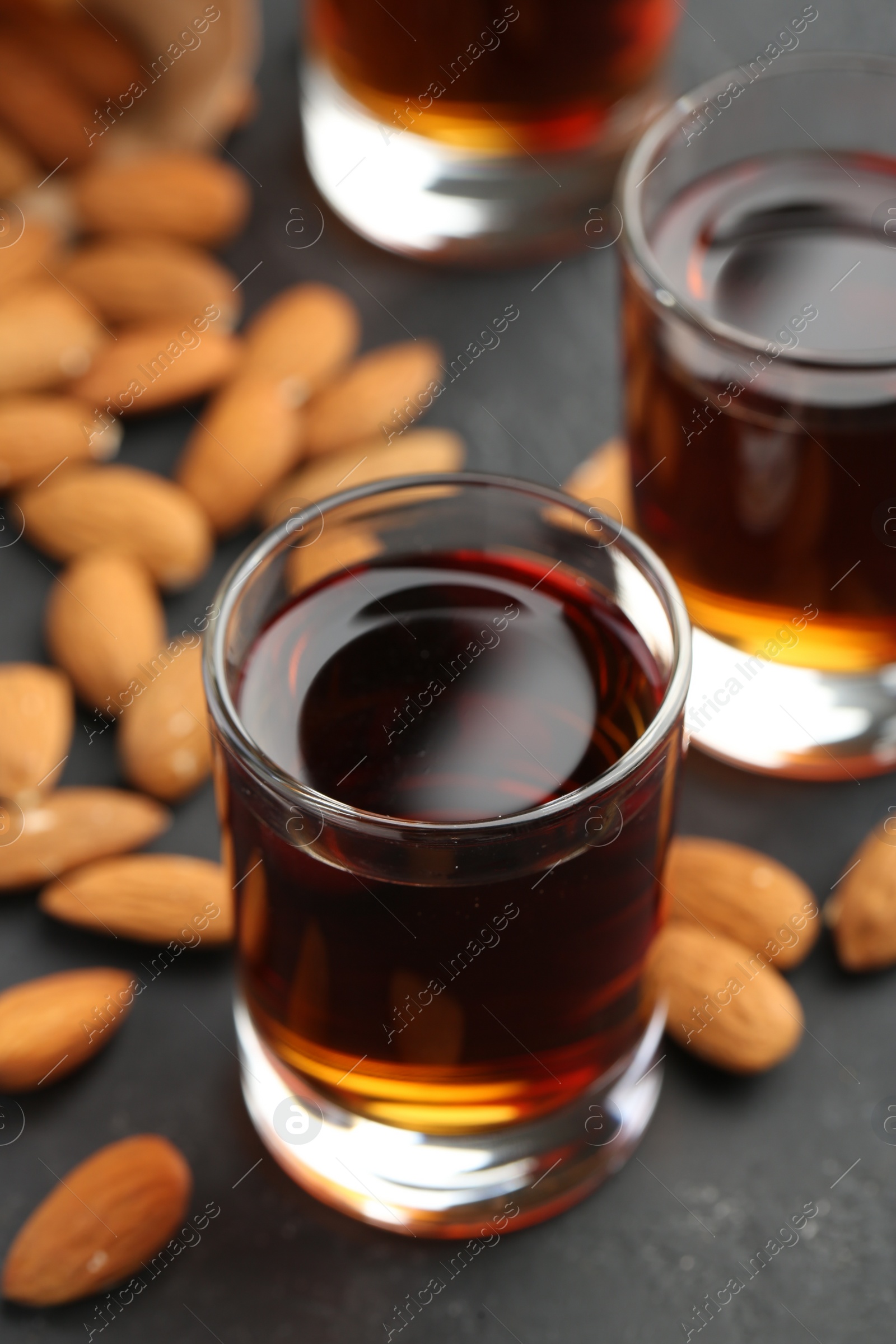 Photo of Glasses with tasty amaretto liqueur and almonds on dark gray table, closeup