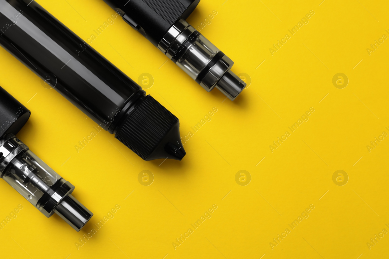 Photo of Electronic cigarettes and vaping liquid on yellow background, flat lay. Space for text