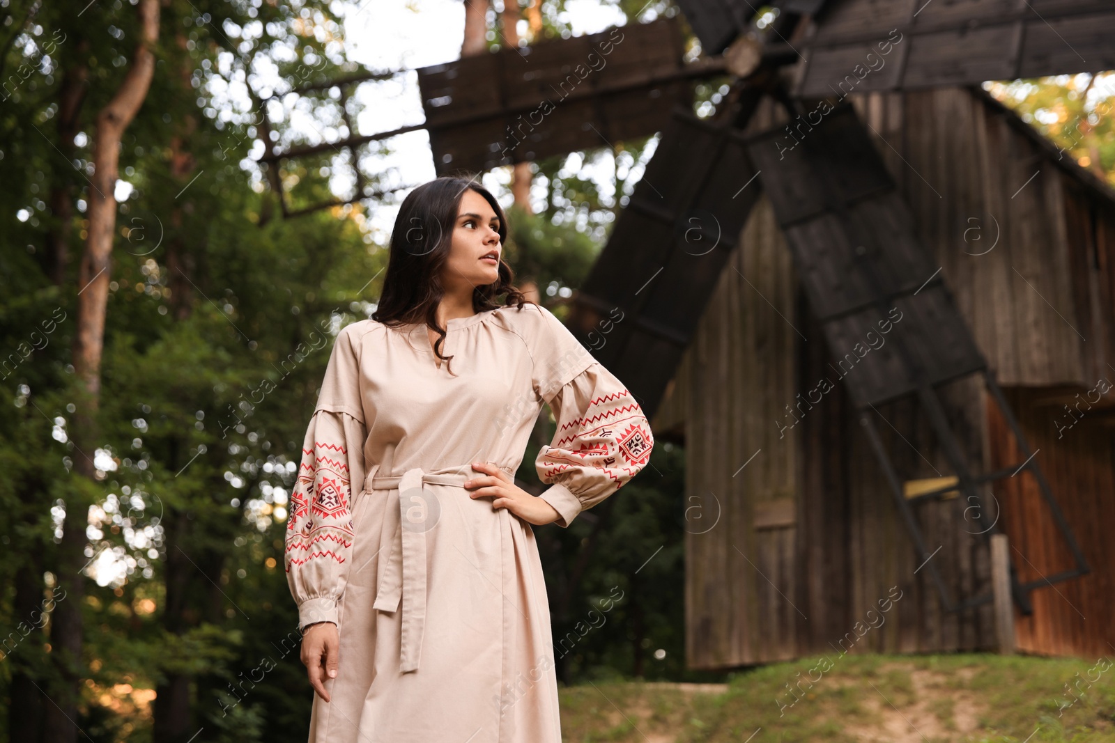 Photo of Beautiful woman wearing embroidered dress near old wooden mill in countryside. Ukrainian national clothes