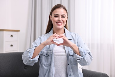 Happy woman showing heart gesture with hands at home