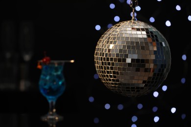 Shiny disco ball hanging over bar counter with cocktail in nightclub, space for text