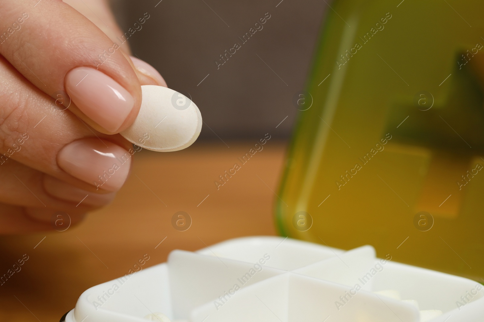 Photo of Woman taking pill from plastic box at table, closeup