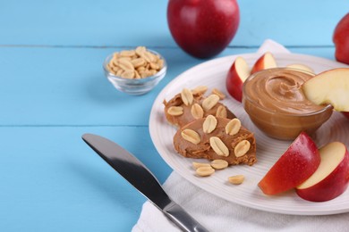 Photo of Slices of fresh apple with peanut butter, nuts and knife on light blue wooden table, closeup