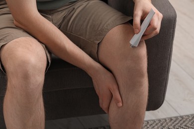 Man applying ointment from tube onto his knee indoors, closeup