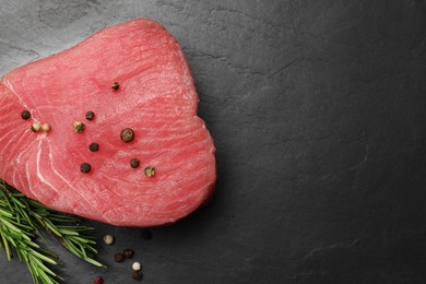 Photo of Raw tuna fillet with peppercorns and rosemary on black table, flat lay. Space for text