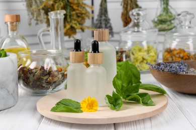 Photo of Bottles of essential oils, leaves, flower and herbs on white wooden table