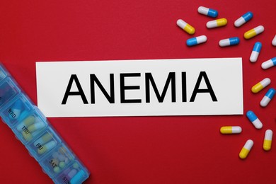 Photo of Card with word Anemia and pills on red background, flat lay