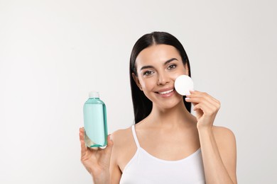 Photo of Young woman with micellar water and cotton pad on light grey background