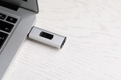 Modern usb flash drive attached into laptop on white wooden table, above view. Space for text