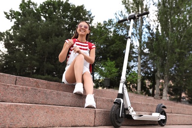 Young woman with electric kick scooter on stairs outdoors