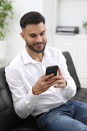 Handsome young man using smartphone on sofa in office