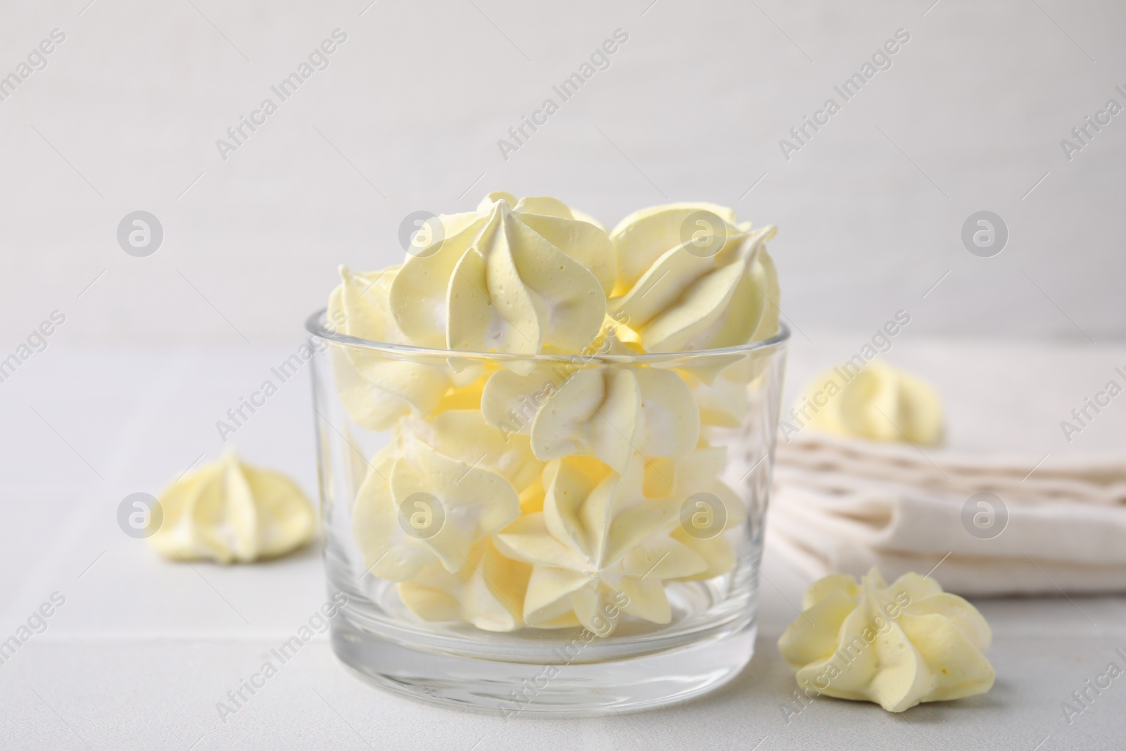 Photo of Tasty meringue cookies in glass on white tiled table