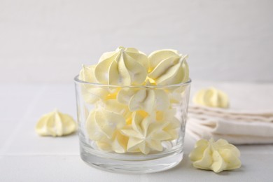 Photo of Tasty meringue cookies in glass on white tiled table