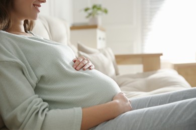 Photo of Pregnant woman touching her belly indoors, closeup