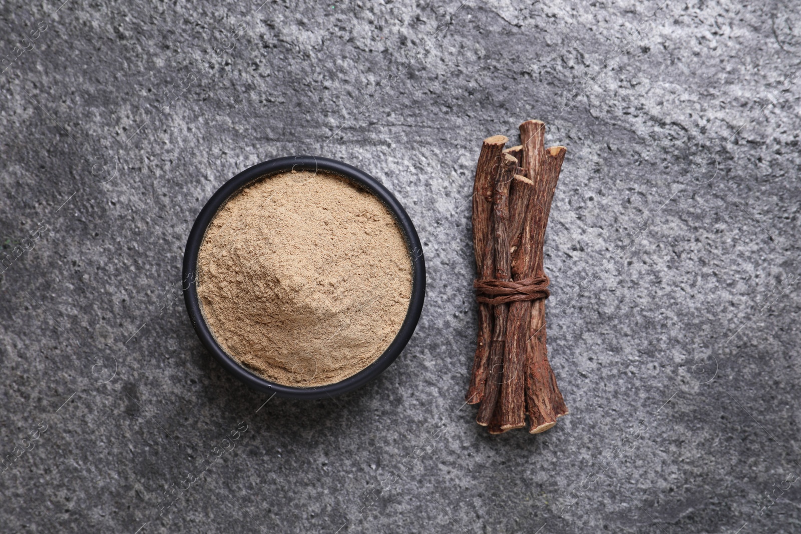 Photo of Powder in bowl and dried sticks of liquorice root on grey table, flat lay