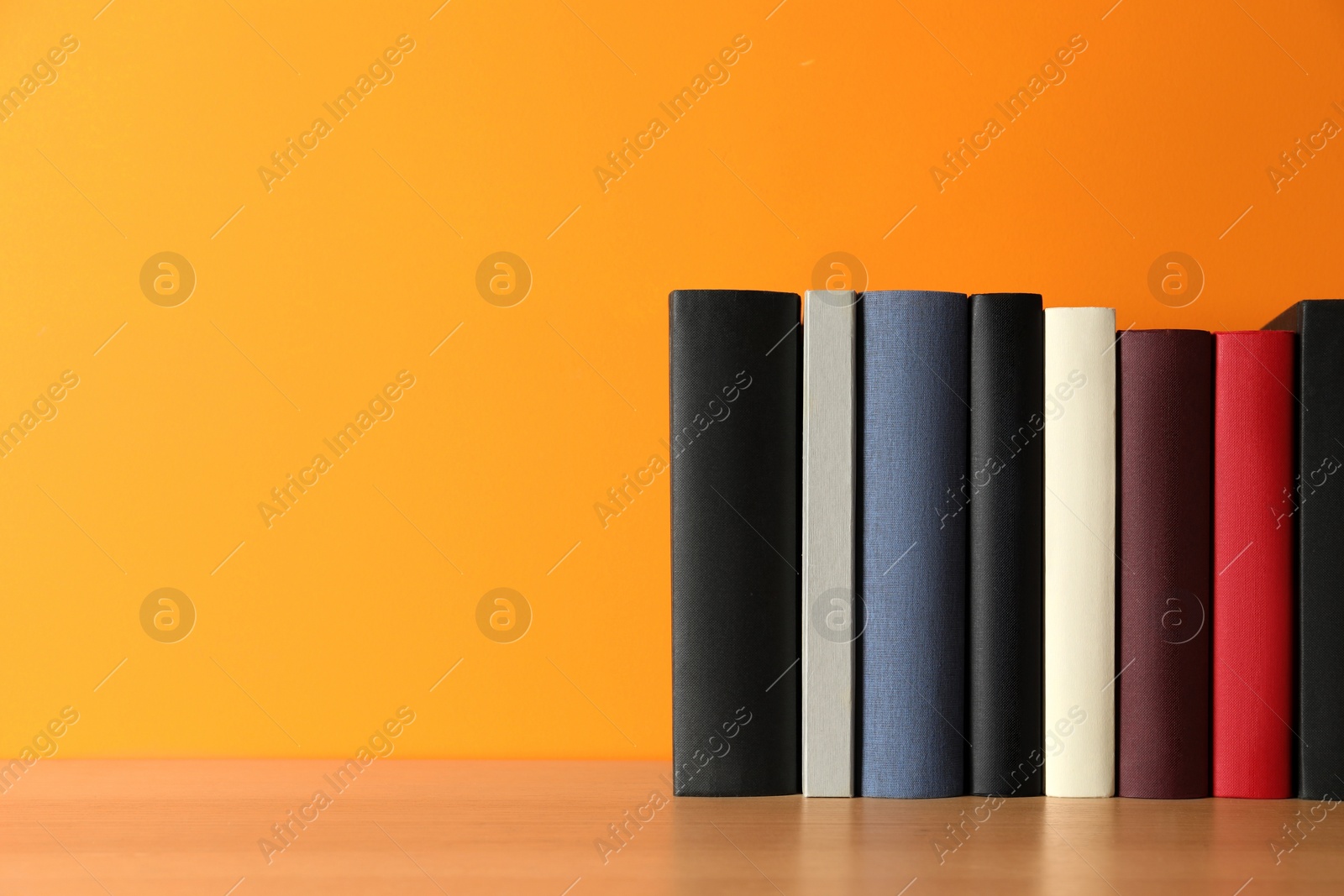 Photo of Many books on wooden table near orange wall, space for text