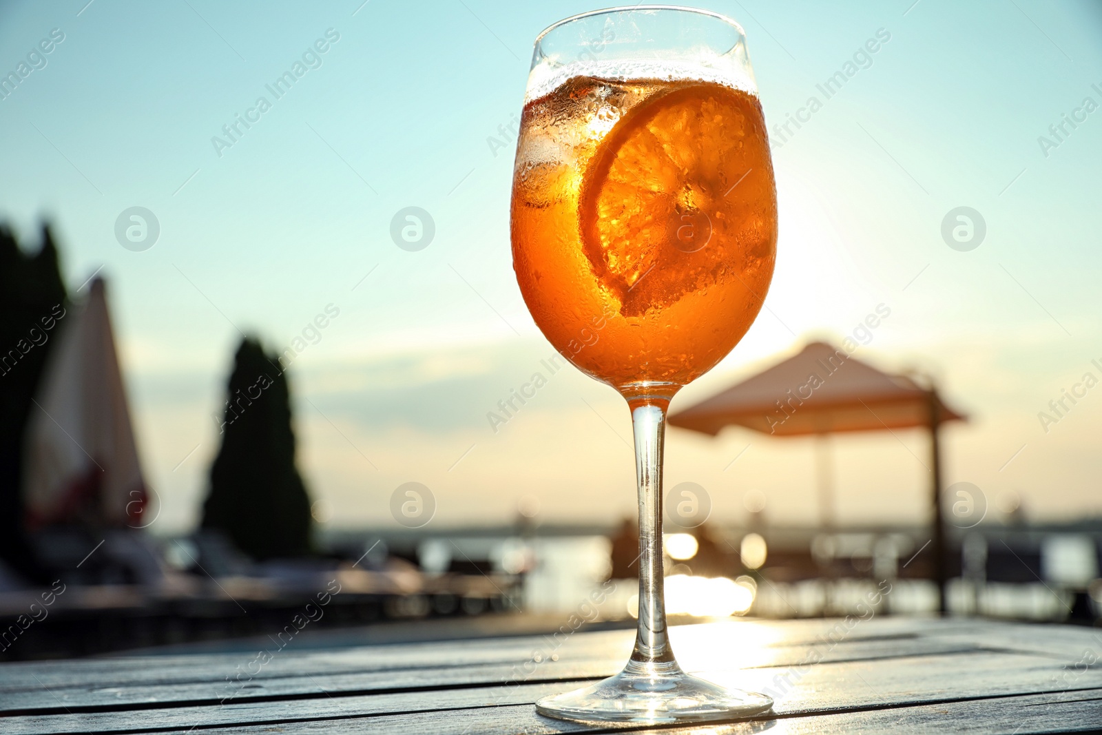 Photo of Glass of fresh summer cocktail on wooden table outdoors at sunset, low angle view
