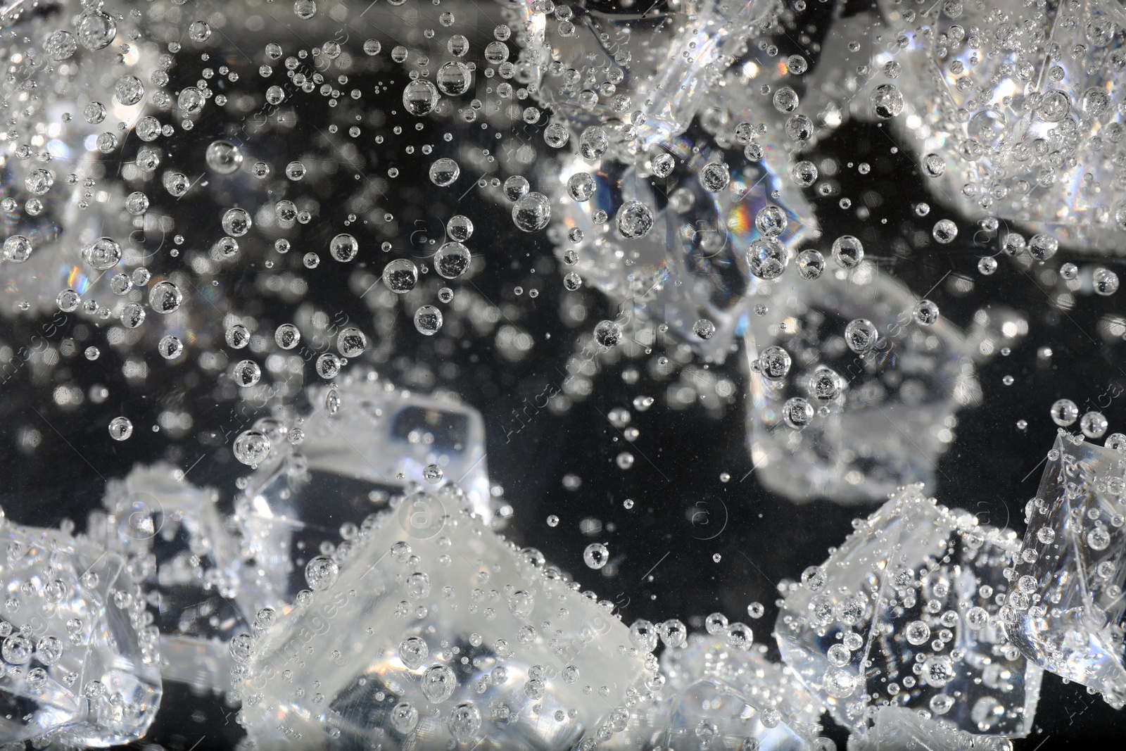 Photo of Clear soda water with ice cubes against black background, closeup