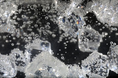 Clear soda water with ice cubes against black background, closeup