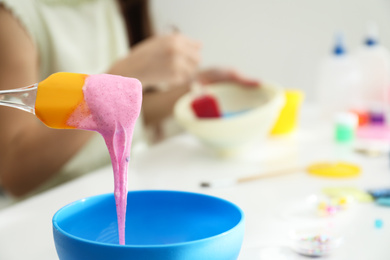 Photo of Pink slime pouring into bowl on white table, closeup. Handmade toy