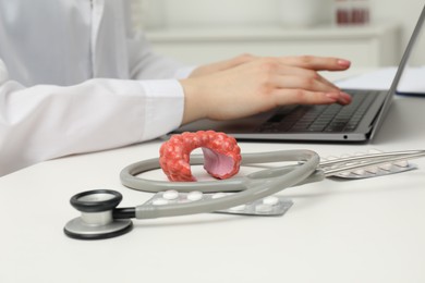 Photo of Endocrinologist working at table, focus on stethoscope and model of thyroid gland