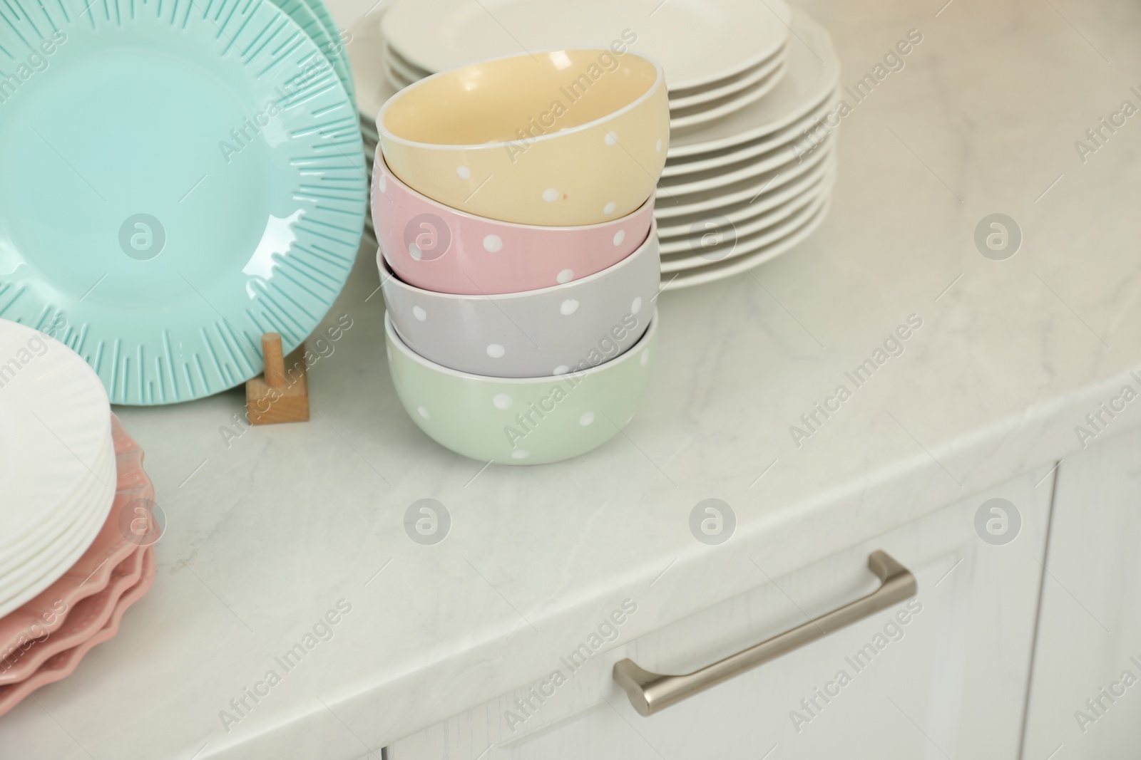 Photo of Clean plates and bowls on white marble countertop in kitchen