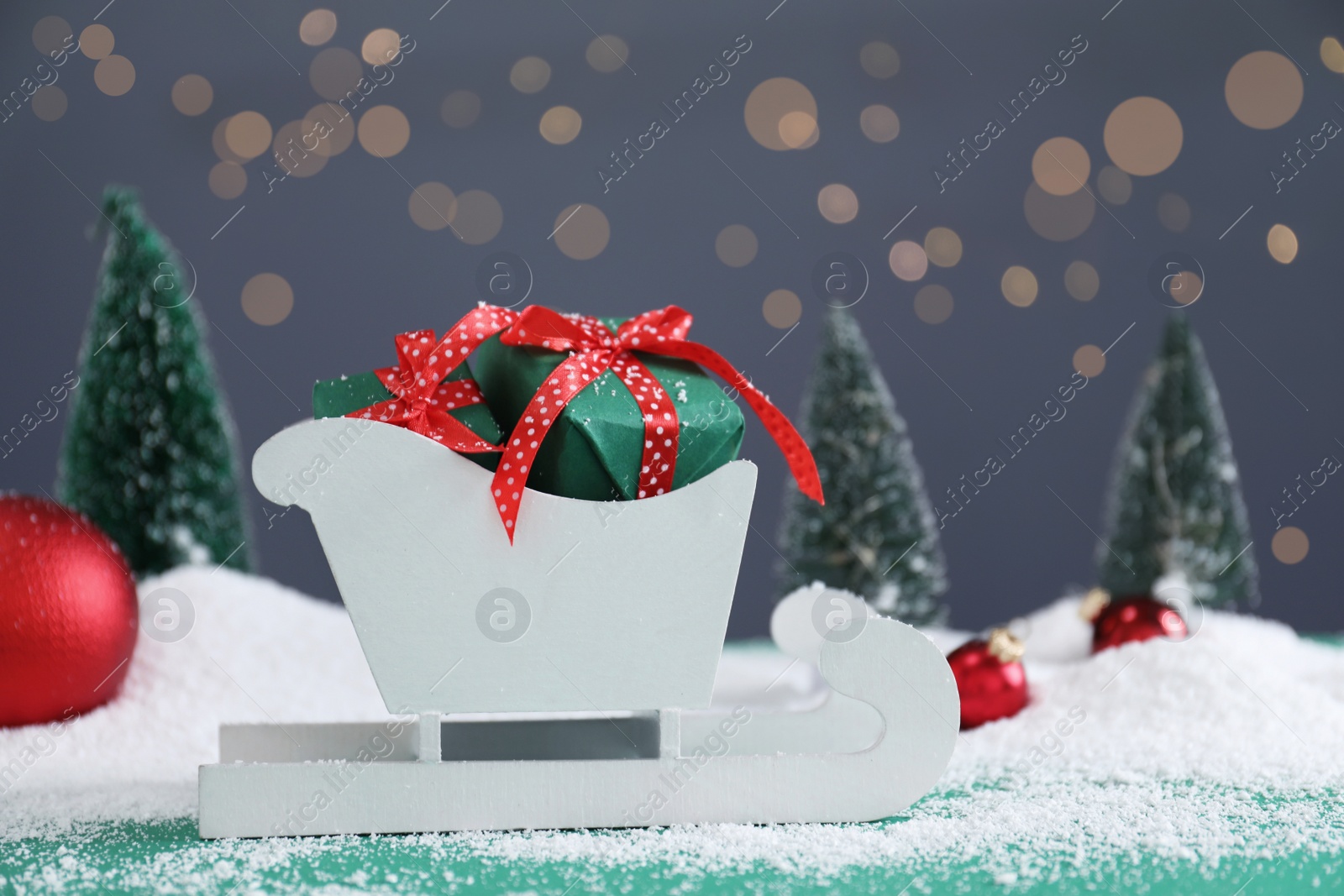 Photo of Sleigh with gift boxes on turquoise wooden table, bokeh effect