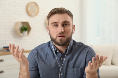 Photo of Young man with earphones holding online webinar indoors, view from webcam