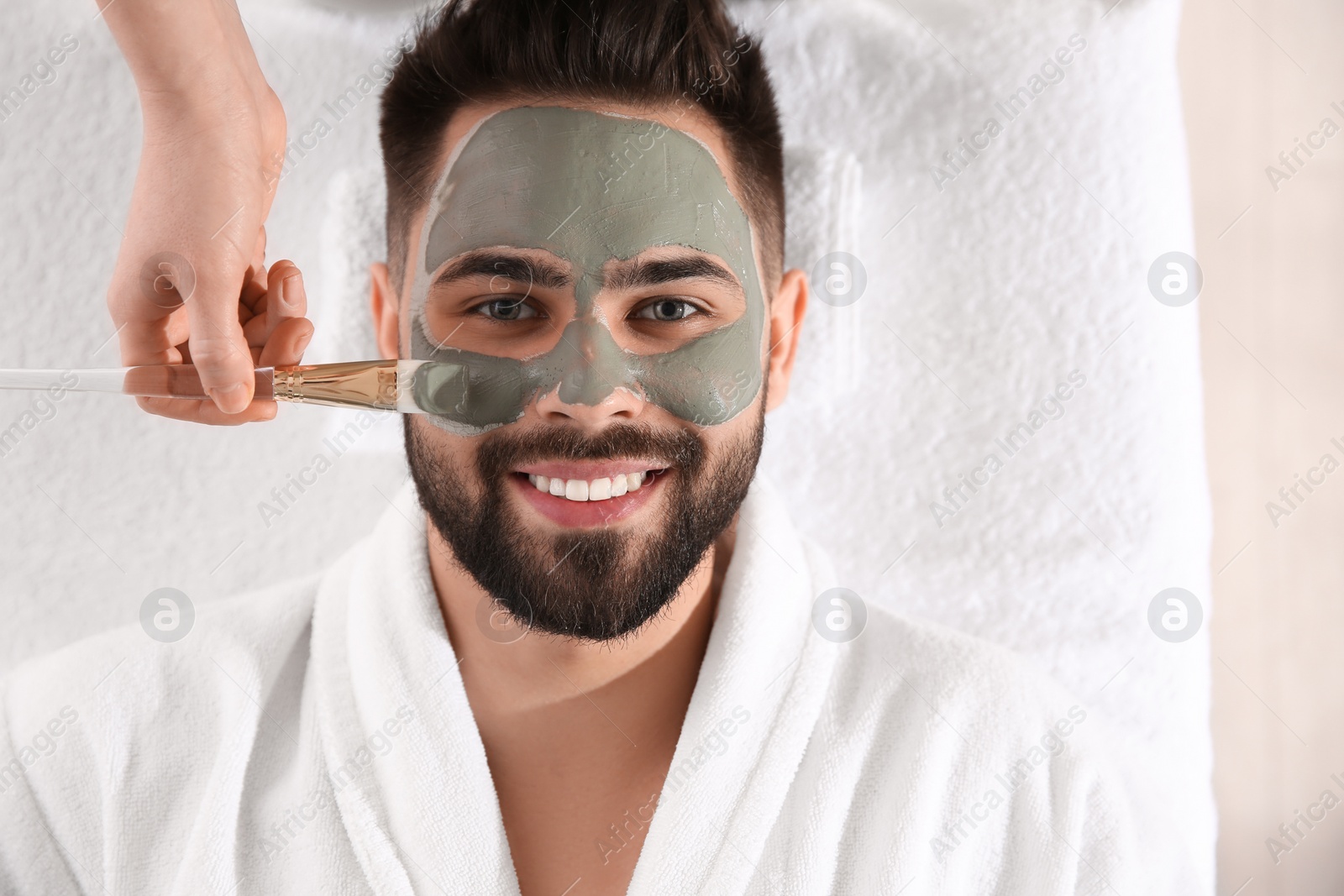 Photo of Cosmetologist applying mask on man's face in spa salon, top view