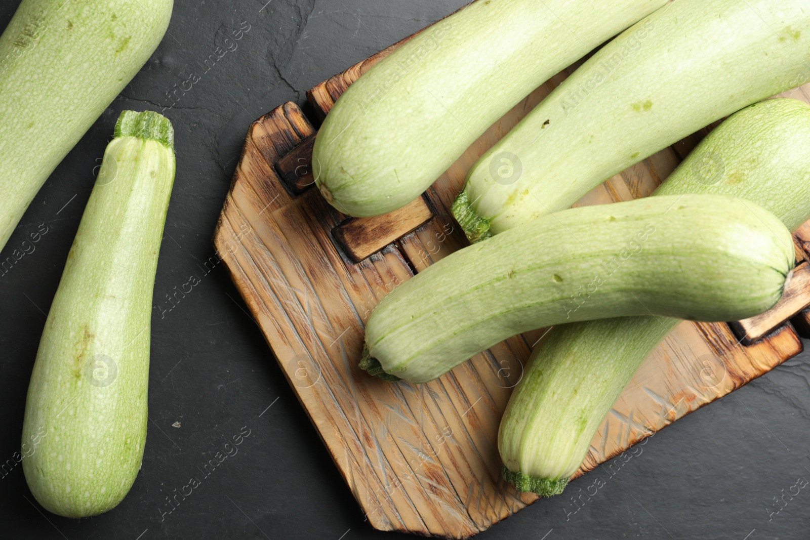 Photo of Raw green zucchinis and wooden board on black slate table, flat lay