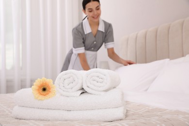 Photo of Chambermaid making bed in hotel room, focus on fresh towels