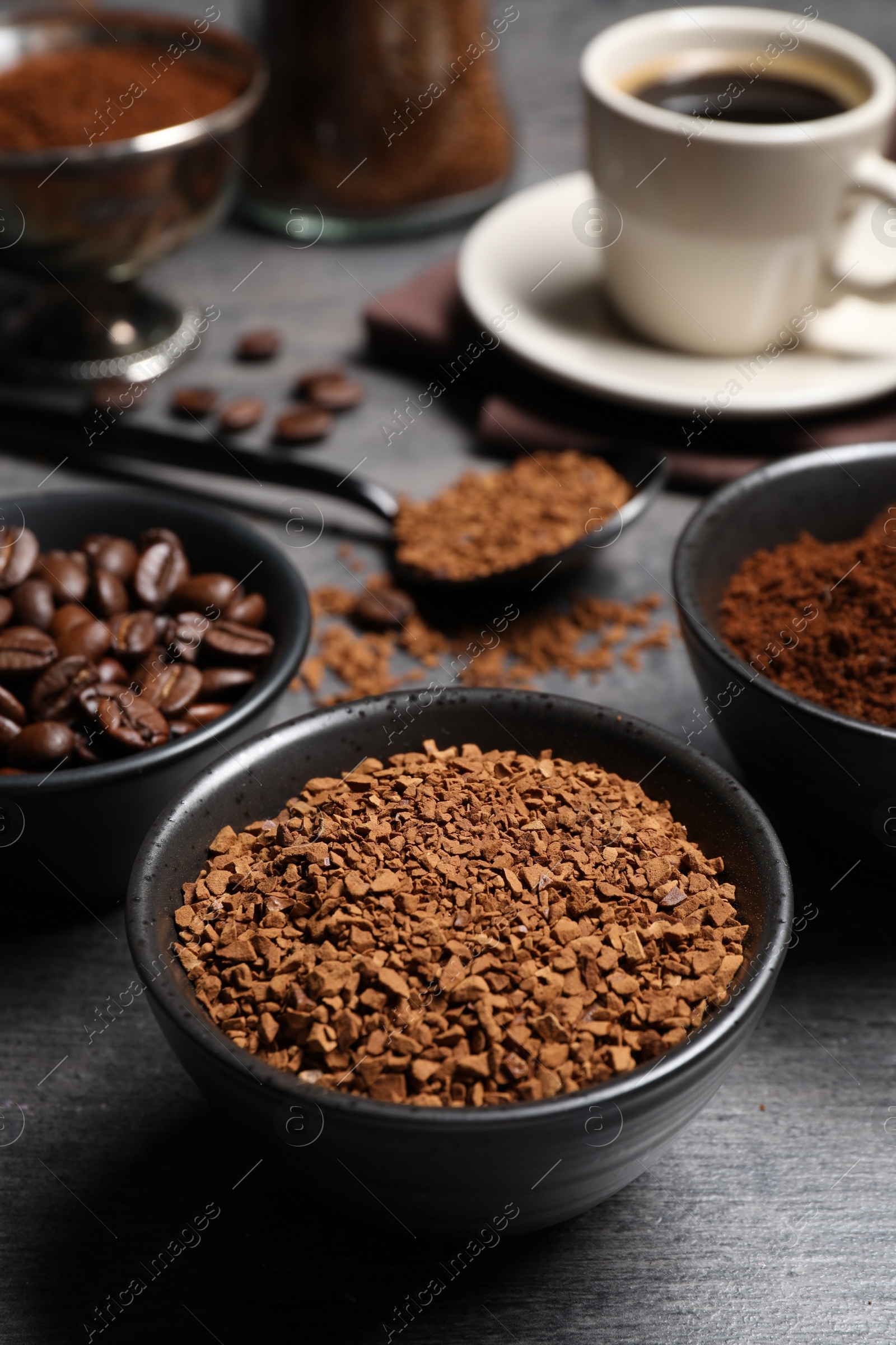 Photo of Bowls of beans, instant and ground coffee on grey table