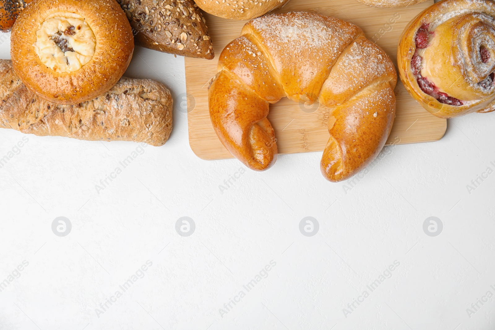 Photo of Fresh breads and pastries on white table, flat lay. Space for text