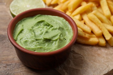 Photo of Delicious french fries, avocado dip and lime on parchment, closeup