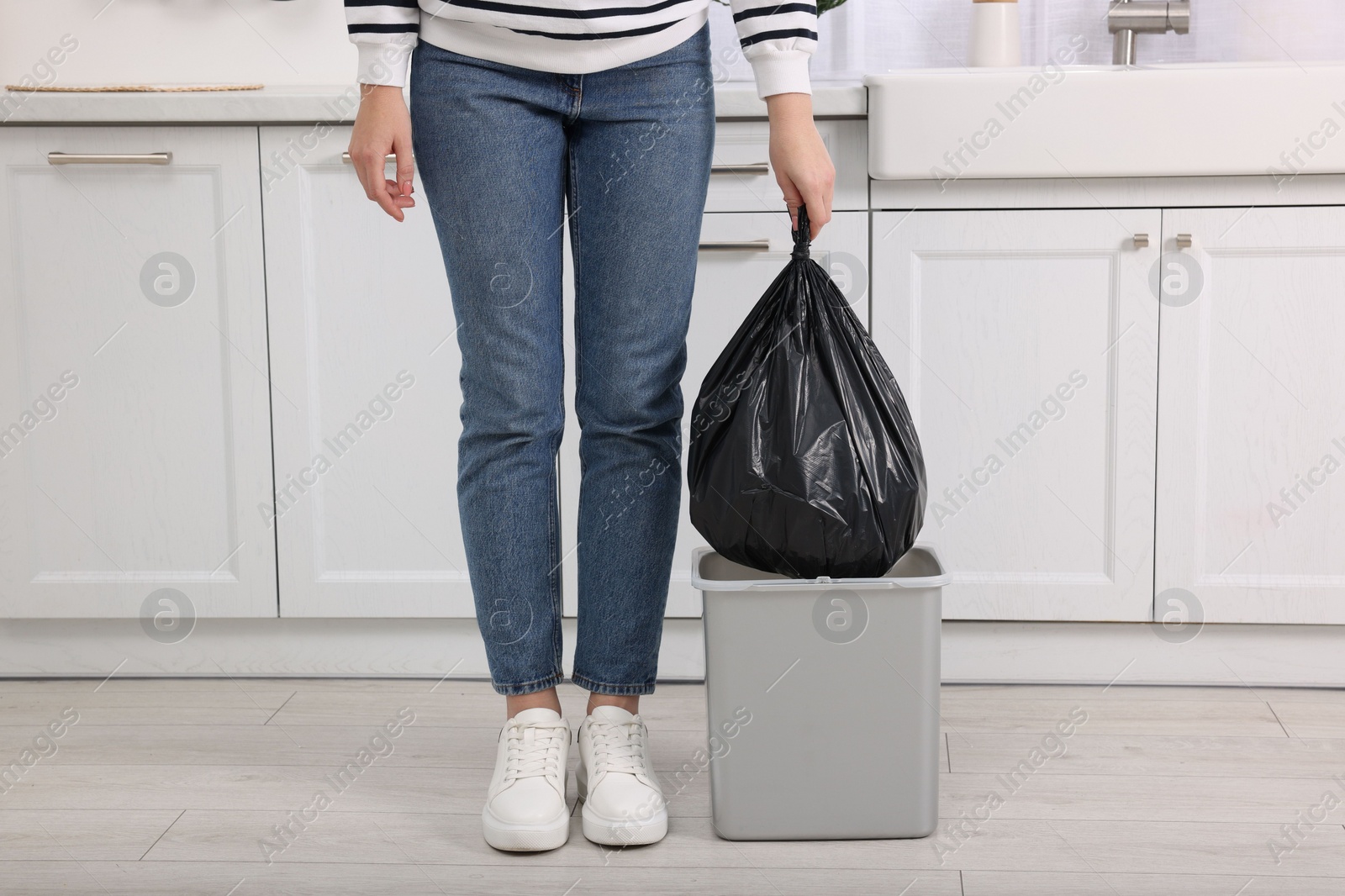 Photo of Woman taking garbage bag out of trash bin in kitchen, closeup