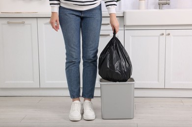 Photo of Woman taking garbage bag out of trash bin in kitchen, closeup