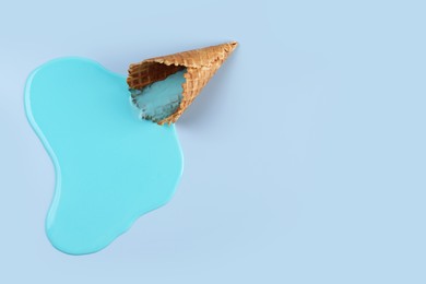 Photo of Melted ice cream and wafer cone on light blue background, top view. Space for text