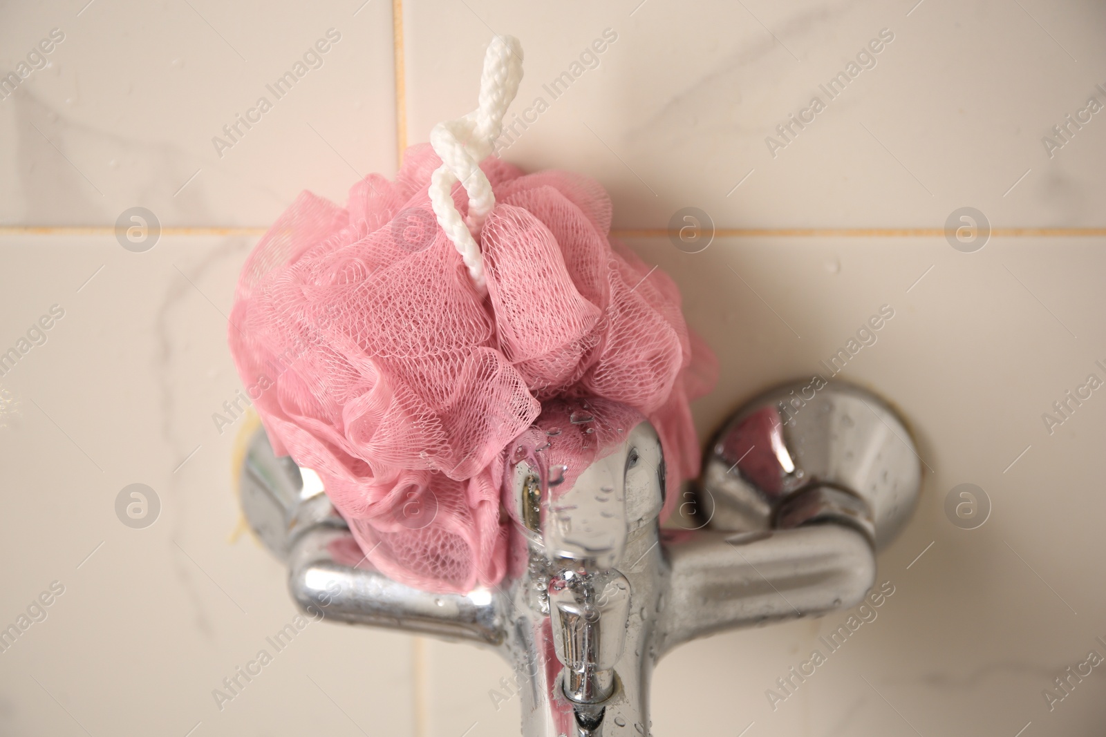 Photo of Pink shower puff on faucet in bathroom, closeup