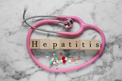 Word Hepatitis made of wooden cubes, stethoscope and pills on white marble table, flat lay