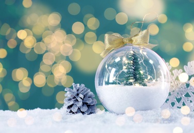 Image of Beautiful transparent Christmas ornament with small fir tree on snow against blurred lights, bokeh effect. Space for text