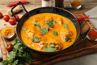 Photo of Tasty chicken curry with parsley and ingredients on wooden table