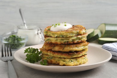 Photo of Delicious zucchini fritters with sour cream on grey table