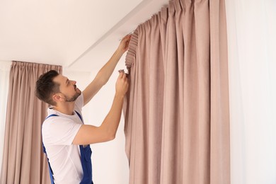Worker in uniform hanging window curtain indoors