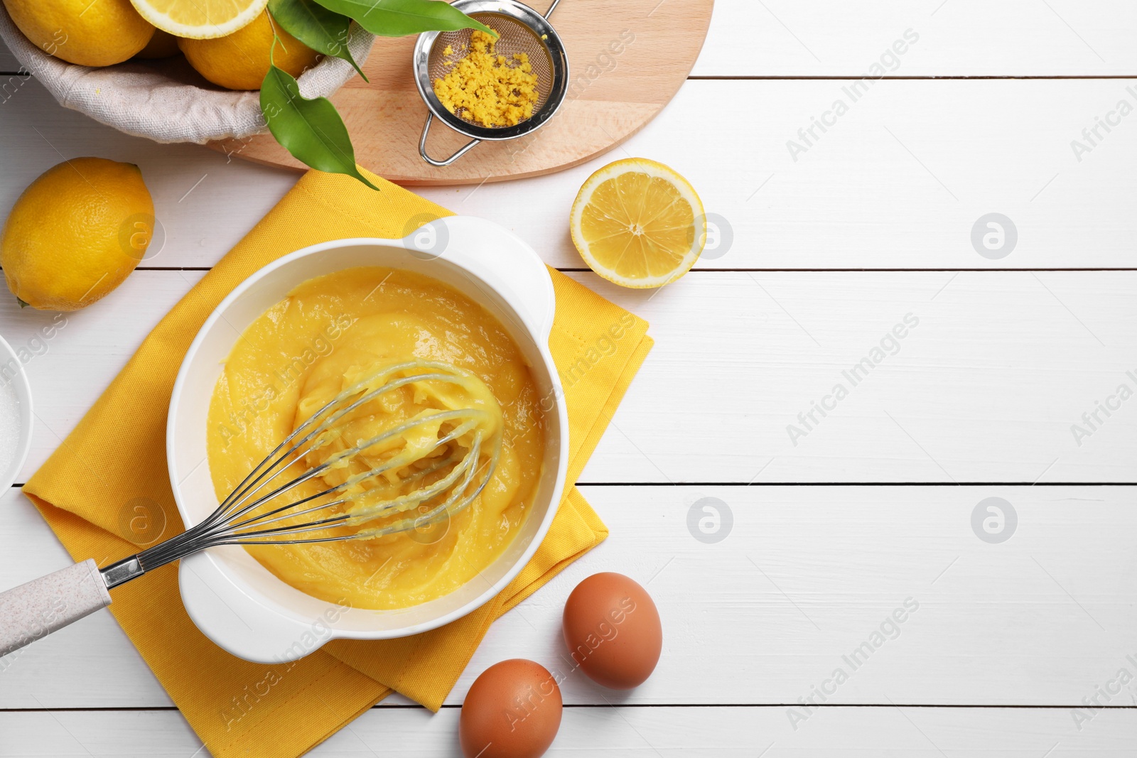 Photo of Delicious lemon curd in bowl, ingredients, whisk and sieve on white wooden table, flat lay. Space for text