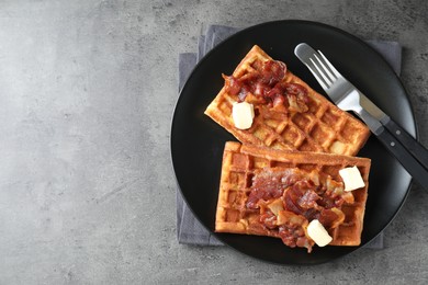 Photo of Tasty Belgian waffles served with bacon and butter on grey table, top view. Space for text