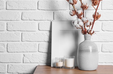 Cotton branches with fluffy flowers in vase on wooden table near white brick wall. Space for text